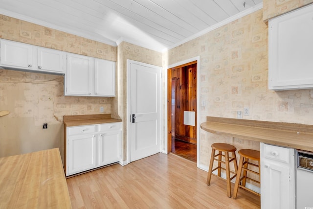 kitchen with light wood-type flooring, wood counters, ornamental molding, and white cabinets