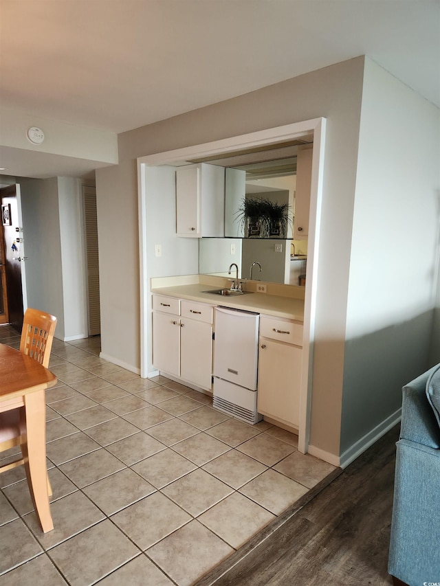 kitchen with light tile patterned floors, sink, dishwashing machine, and white cabinets