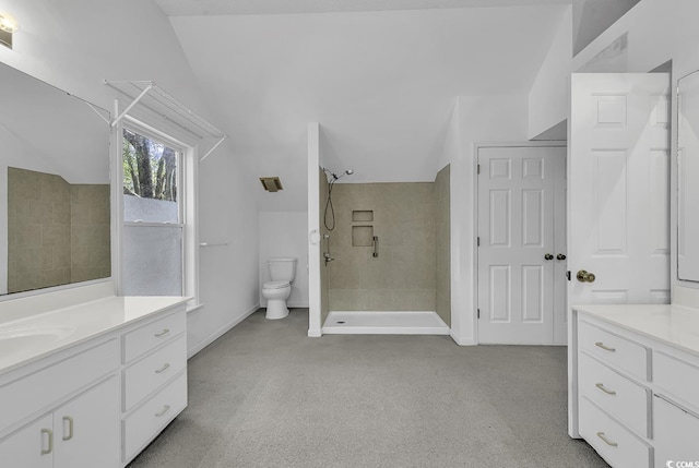 bathroom with tiled shower, vanity, lofted ceiling, and toilet