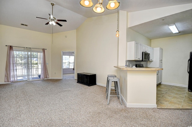 kitchen with light colored carpet, visible vents, white cabinets, tasteful backsplash, and stainless steel microwave