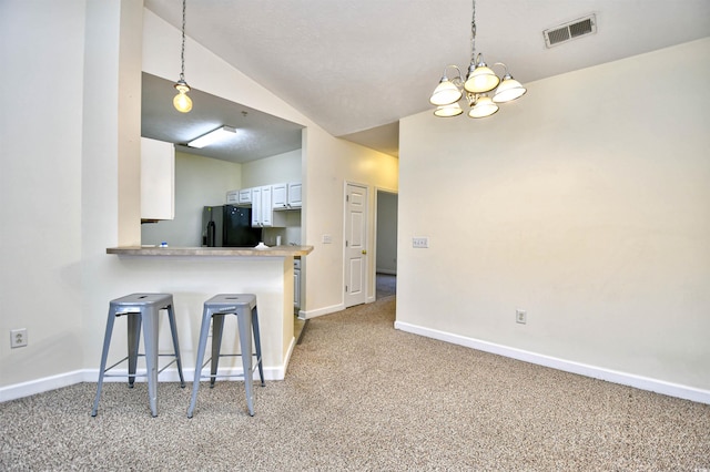 kitchen featuring visible vents, light colored carpet, vaulted ceiling, black refrigerator with ice dispenser, and a kitchen bar