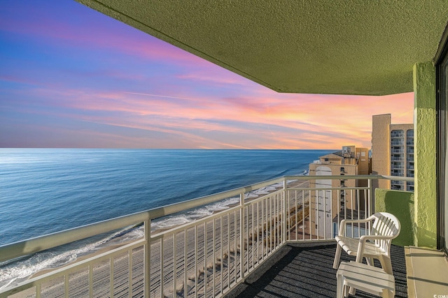 balcony at dusk featuring a water view