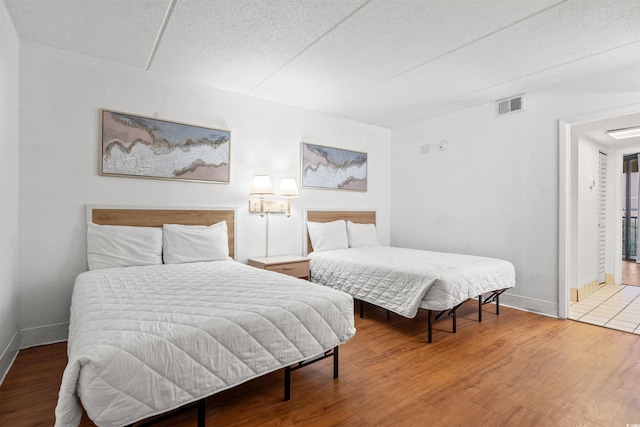 bedroom with wood finished floors, visible vents, and baseboards