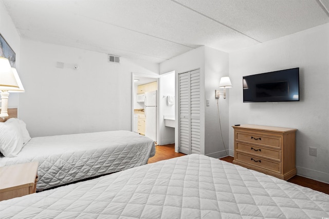 bedroom with visible vents, wood finished floors, freestanding refrigerator, ensuite bathroom, and a textured ceiling