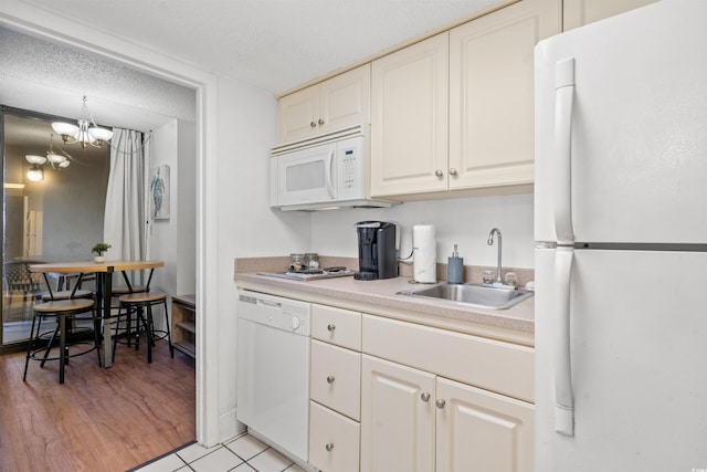 kitchen with white appliances, a sink, white cabinetry, light countertops, and an inviting chandelier