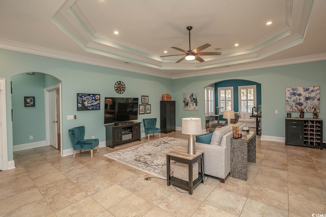 living room with ceiling fan, a tray ceiling, and ornamental molding