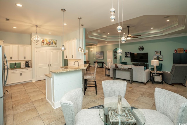 dining room with sink, a tray ceiling, light tile patterned flooring, ornamental molding, and ceiling fan with notable chandelier