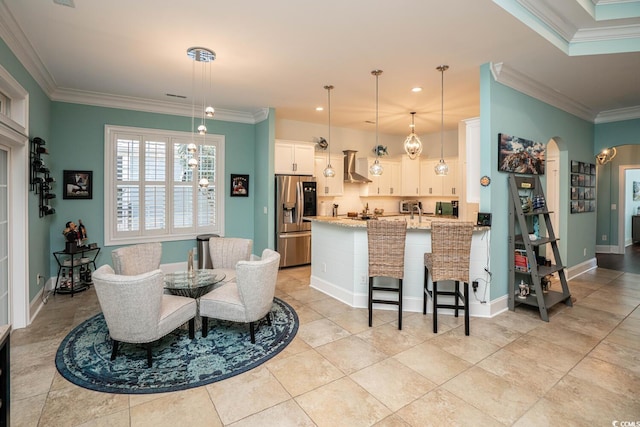 kitchen with stainless steel fridge with ice dispenser, white cabinetry, decorative light fixtures, wall chimney range hood, and light stone counters