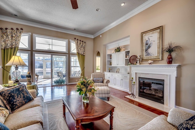 living room with a premium fireplace, built in features, a textured ceiling, ornamental molding, and light hardwood / wood-style flooring