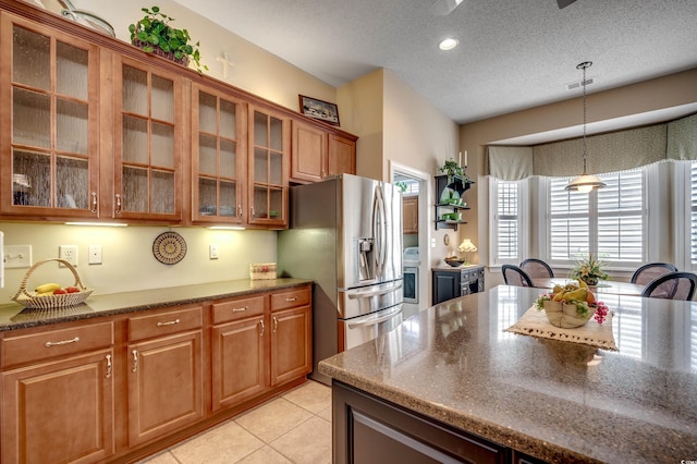 kitchen with dark stone countertops, light tile patterned flooring, hanging light fixtures, stainless steel fridge with ice dispenser, and a textured ceiling