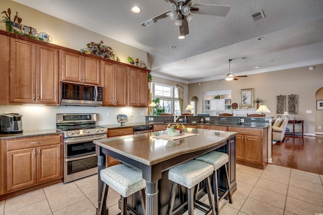 kitchen with a center island, a kitchen breakfast bar, a textured ceiling, stainless steel appliances, and light tile patterned floors