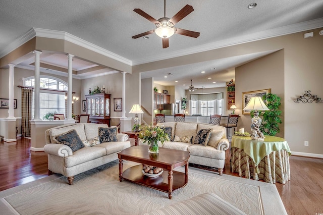 living room with decorative columns, a textured ceiling, ornamental molding, and light wood-type flooring