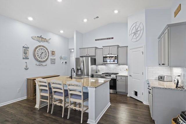 kitchen with vaulted ceiling, a kitchen island with sink, light stone countertops, gray cabinetry, and stainless steel appliances