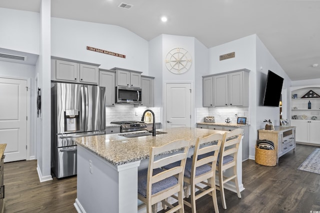 kitchen featuring light stone countertops, appliances with stainless steel finishes, lofted ceiling, sink, and a kitchen island with sink