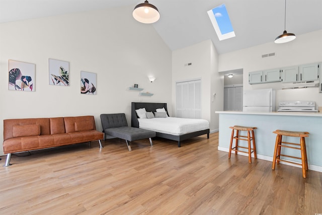 bedroom featuring white fridge, a skylight, light hardwood / wood-style floors, a closet, and high vaulted ceiling