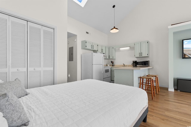 bedroom featuring white fridge, a skylight, light wood-type flooring, high vaulted ceiling, and sink