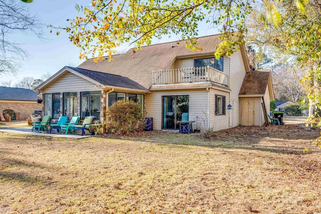 back of house featuring a balcony, a sunroom, a patio area, and a lawn