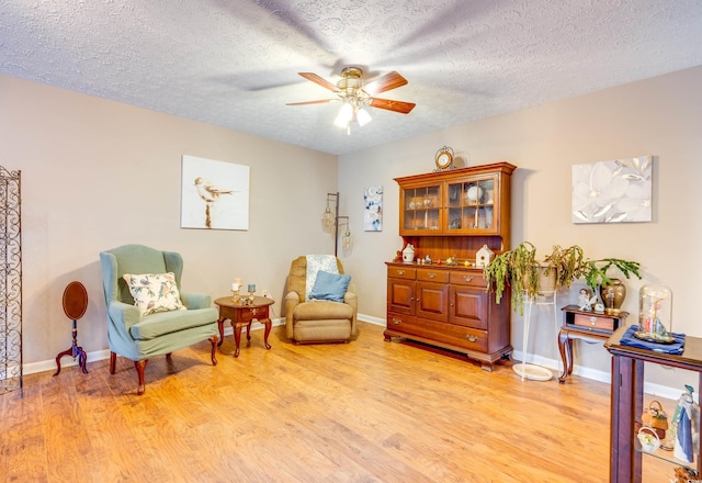 living area with ceiling fan, a textured ceiling, and light hardwood / wood-style flooring