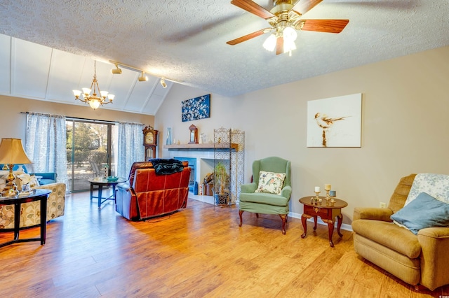 sitting room with lofted ceiling, ceiling fan with notable chandelier, a textured ceiling, and light wood-type flooring