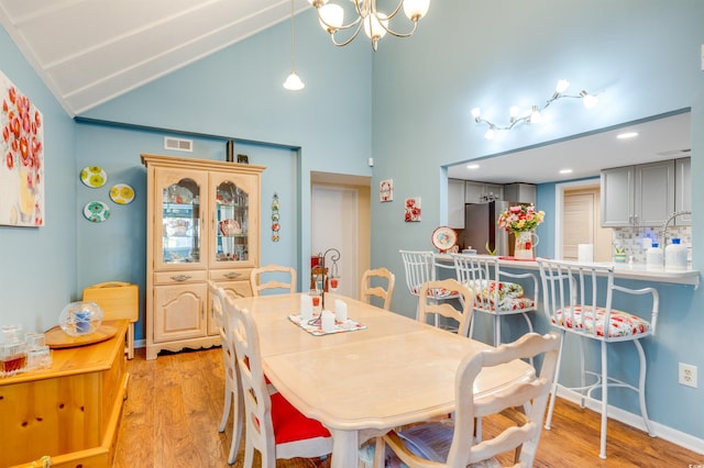 dining room featuring high vaulted ceiling, a chandelier, and light wood-type flooring