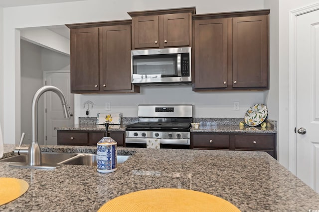 kitchen featuring dark brown cabinets, sink, stainless steel appliances, and dark stone countertops