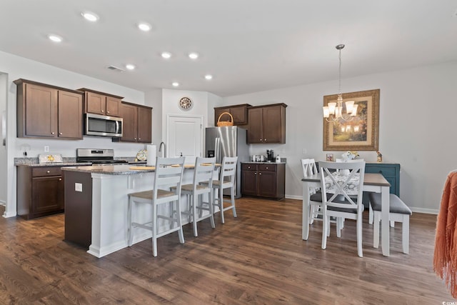 kitchen with dark hardwood / wood-style flooring, stainless steel appliances, hanging light fixtures, a notable chandelier, and a center island with sink