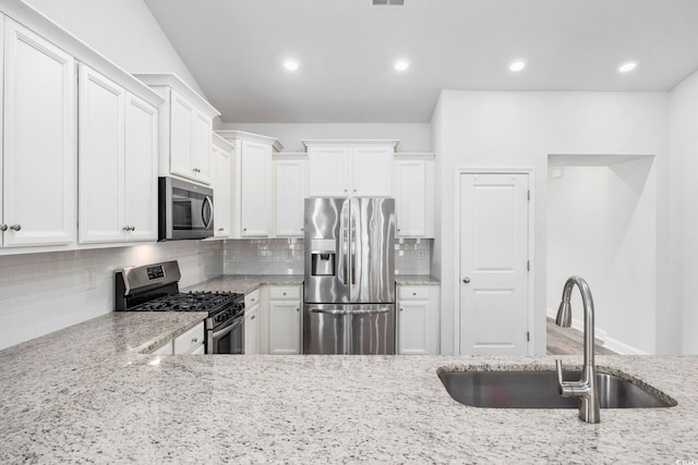 kitchen featuring appliances with stainless steel finishes, tasteful backsplash, white cabinets, light stone counters, and sink