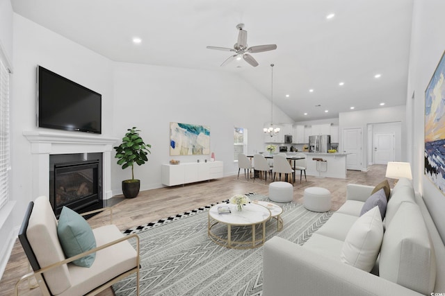 living room with ceiling fan with notable chandelier, light hardwood / wood-style flooring, and lofted ceiling