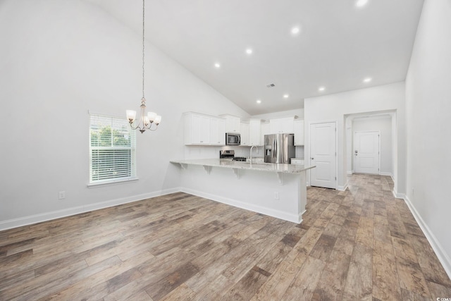 kitchen featuring pendant lighting, white cabinetry, stainless steel appliances, kitchen peninsula, and high vaulted ceiling