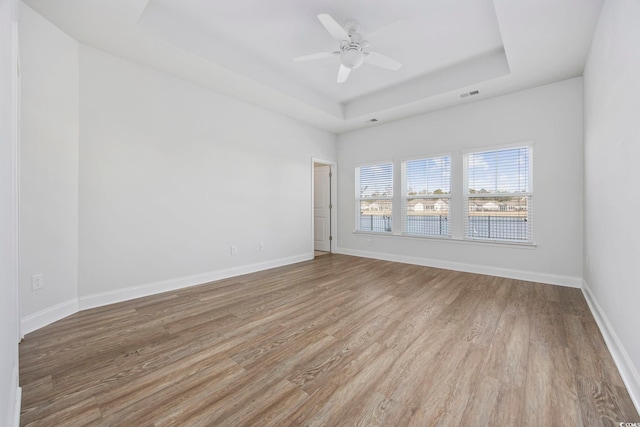 unfurnished room with ceiling fan, light hardwood / wood-style flooring, and a raised ceiling