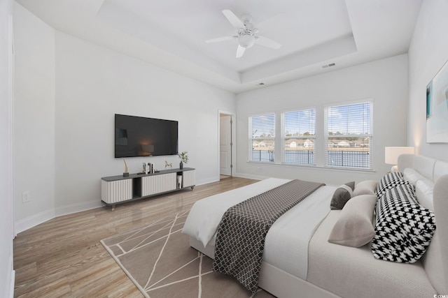 bedroom with ceiling fan, hardwood / wood-style floors, and a tray ceiling