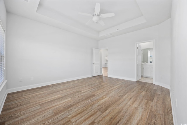 unfurnished bedroom featuring ceiling fan, ensuite bathroom, a raised ceiling, and light wood-type flooring