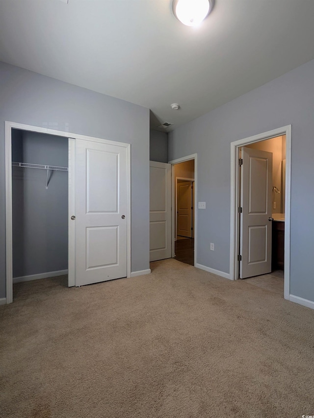 unfurnished bedroom featuring light colored carpet, a closet, and ensuite bath