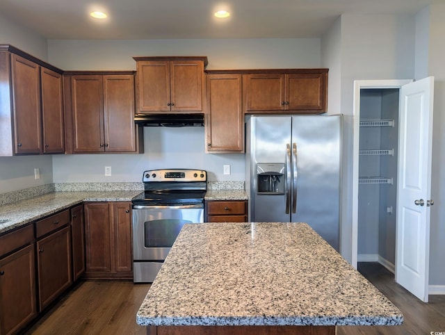 kitchen with dark wood-type flooring, stainless steel appliances, light stone counters, and a kitchen island