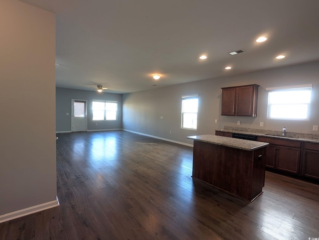 kitchen featuring ceiling fan, dark wood-type flooring, light stone counters, and a kitchen island