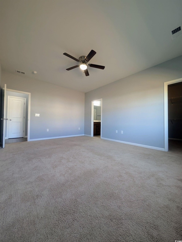 unfurnished bedroom with ceiling fan, a closet, a spacious closet, and light carpet