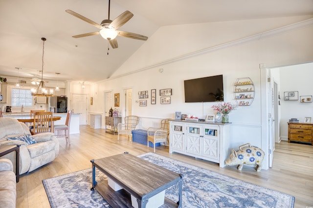 living room with light wood-type flooring, ceiling fan with notable chandelier, and high vaulted ceiling