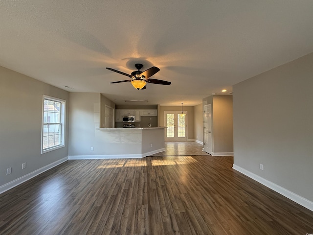 unfurnished living room featuring ceiling fan, dark wood-type flooring, a wealth of natural light, and french doors