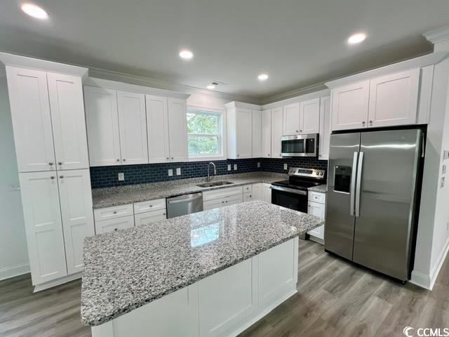 kitchen with a kitchen island, white cabinetry, stainless steel appliances, sink, and light stone counters