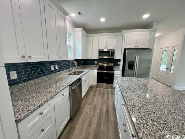 kitchen with white cabinets, stainless steel appliances, decorative backsplash, sink, and light stone counters