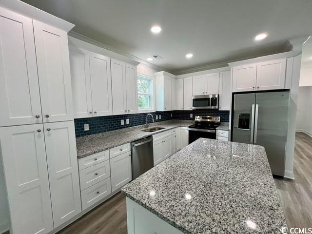 kitchen with stainless steel appliances, tasteful backsplash, white cabinets, a sink, and wood finished floors