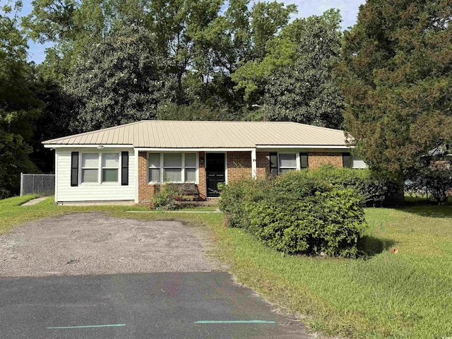 ranch-style house featuring brick siding, fence, metal roof, and a front yard