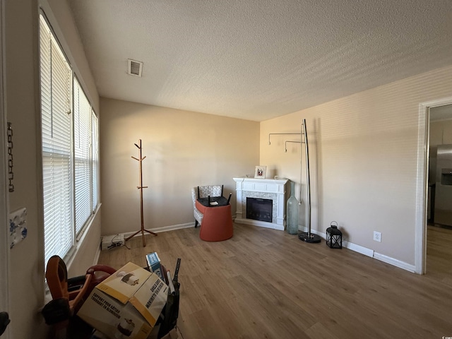 unfurnished living room with a textured ceiling, visible vents, wood finished floors, baseboards, and a glass covered fireplace