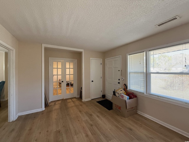 interior space featuring french doors, a textured ceiling, visible vents, baseboards, and light wood-style floors