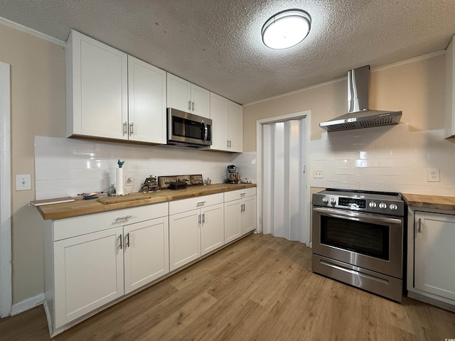 kitchen with wall chimney range hood, crown molding, light wood-style floors, wood counters, and stainless steel appliances