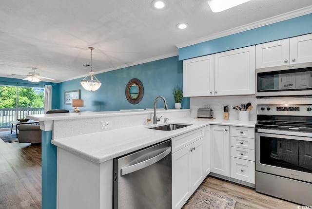 kitchen featuring kitchen peninsula, sink, hanging light fixtures, stainless steel appliances, and white cabinets