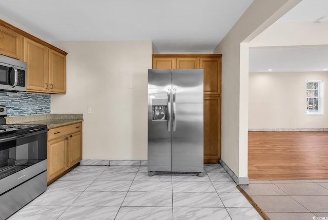 kitchen with backsplash, light tile patterned flooring, light stone counters, and stainless steel appliances