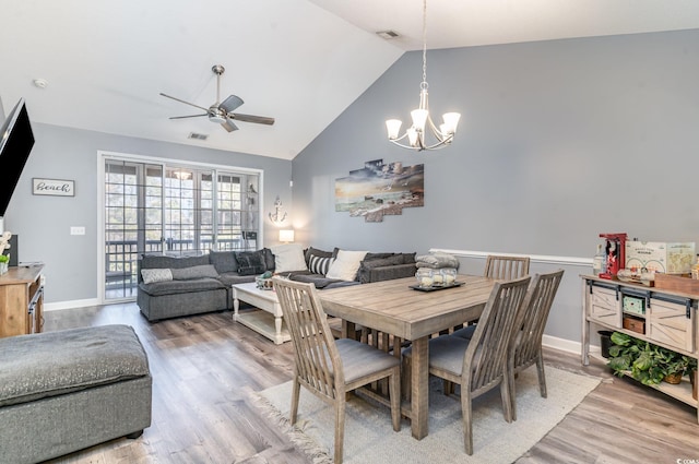 dining room featuring ceiling fan with notable chandelier, wood-type flooring, and high vaulted ceiling