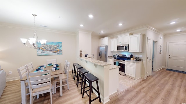 kitchen featuring white cabinetry, hanging light fixtures, stainless steel appliances, a kitchen breakfast bar, and light stone countertops