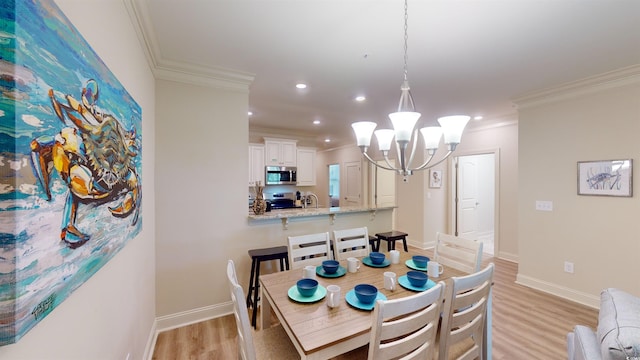 dining area with a notable chandelier, crown molding, sink, and light wood-type flooring